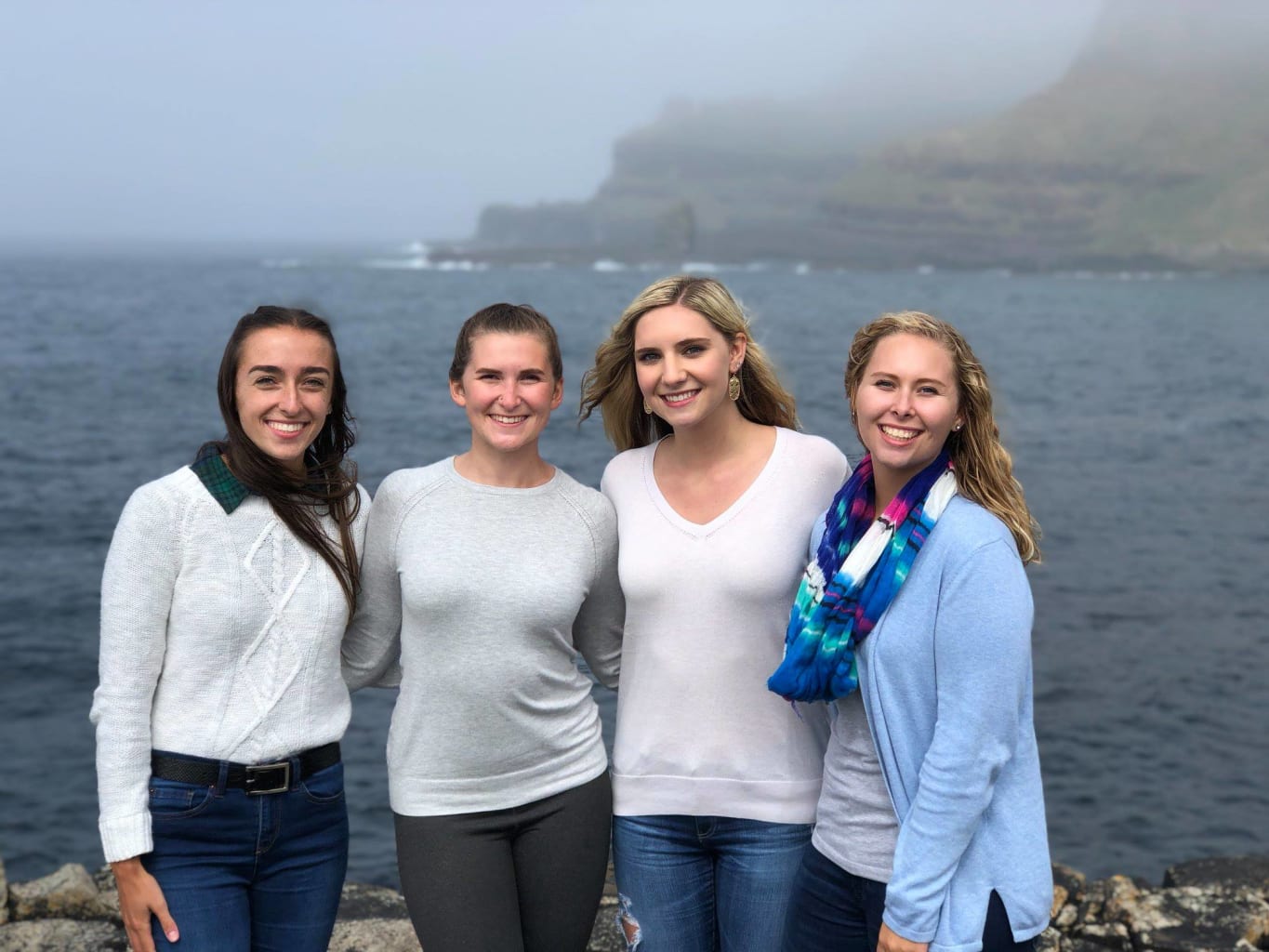 Four girls smiling in front of water.