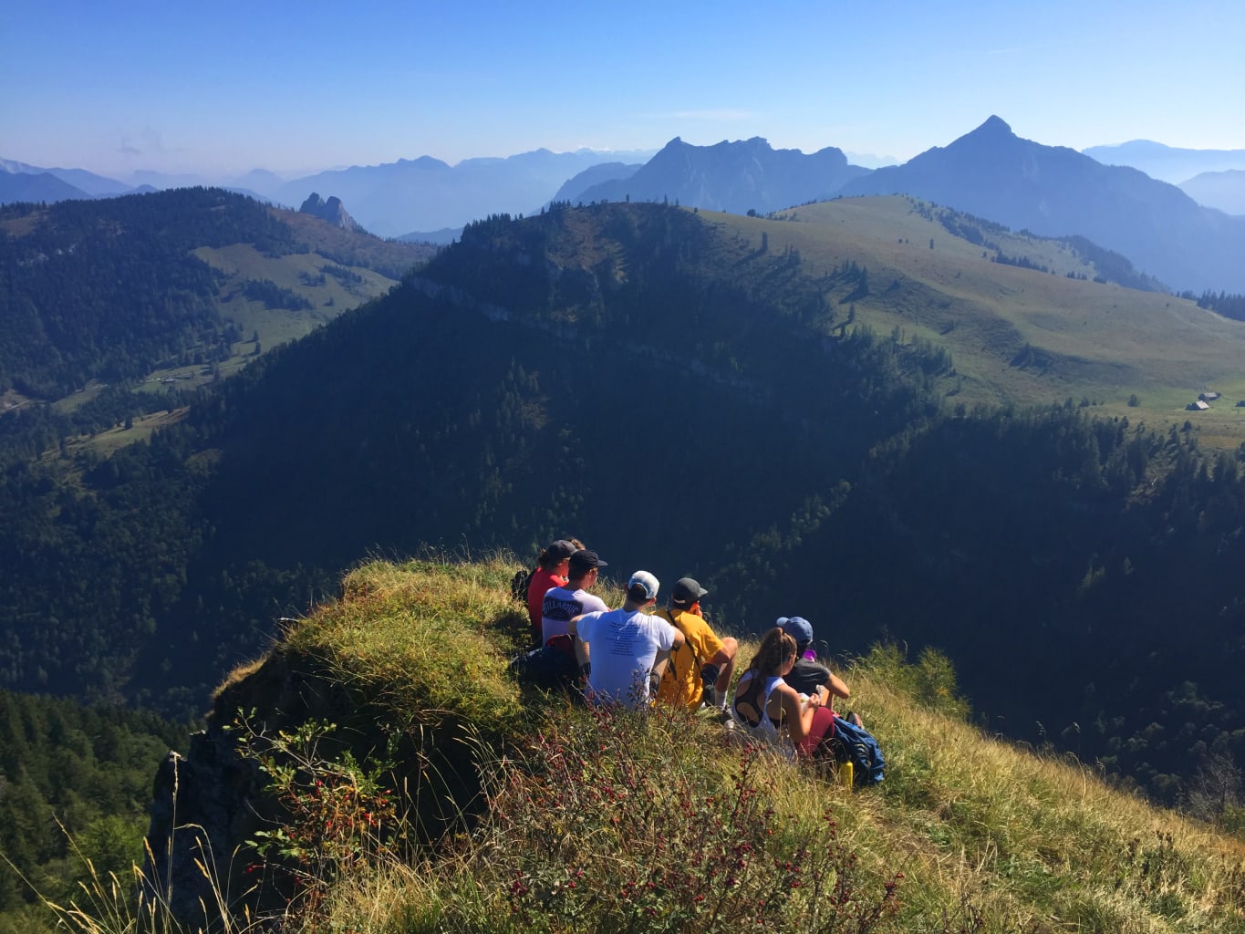 A group of student sitting on a grassy hill overlooking a view of mountains.