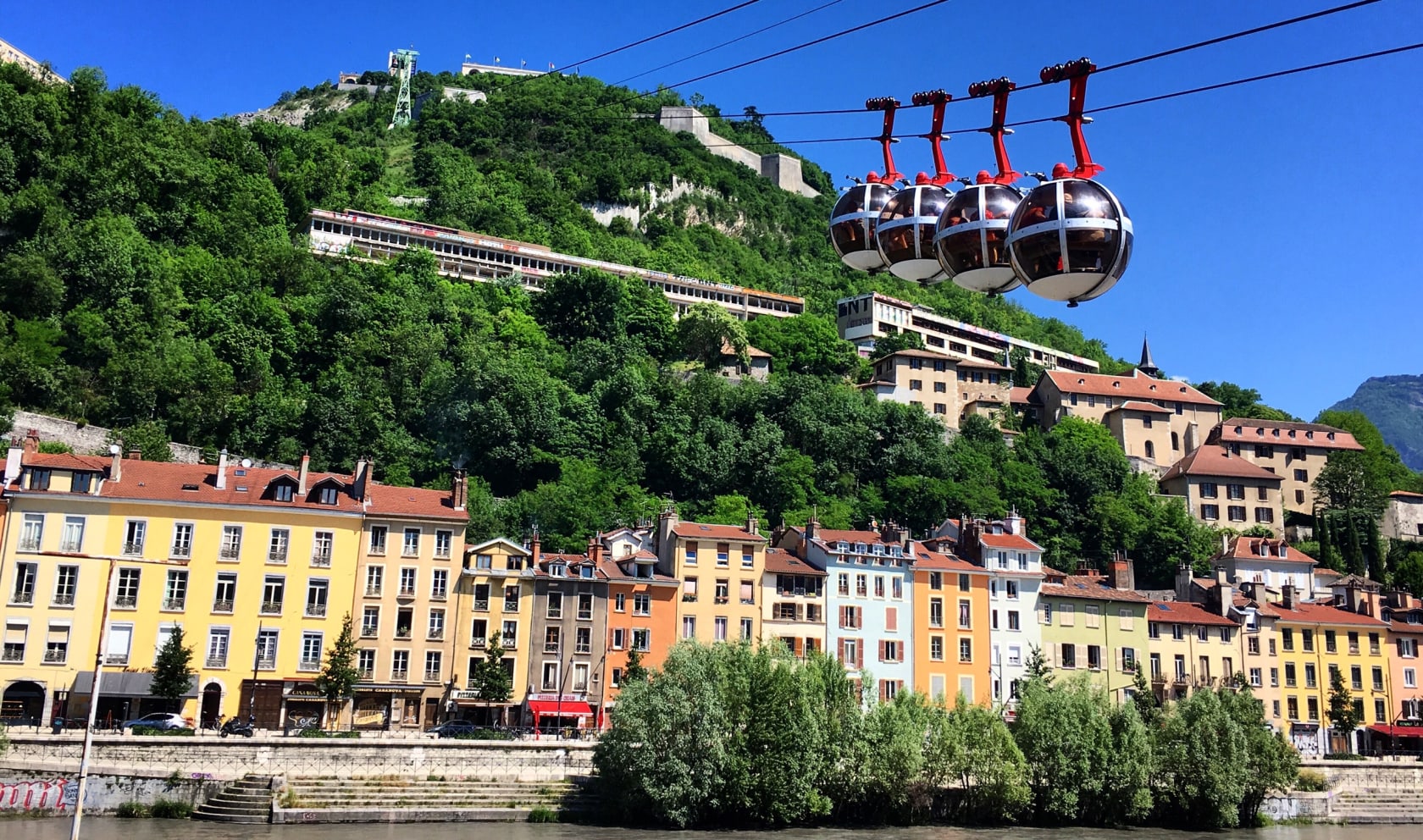 Four cable cars moving up, passing over buildings in Grenoble, France.