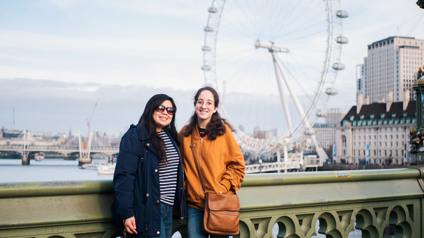 Two students in London, posing on a bridge with a ferris wheel in the background.